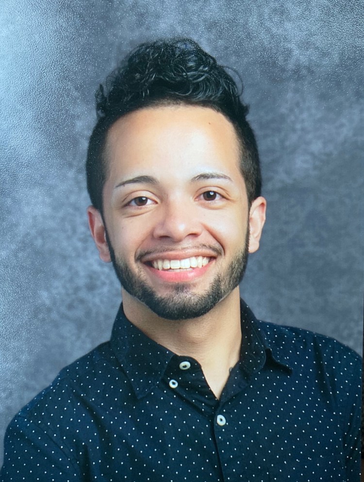 School photo of a smiling Puerto Rican man, a teacher, in a navy blue button down.