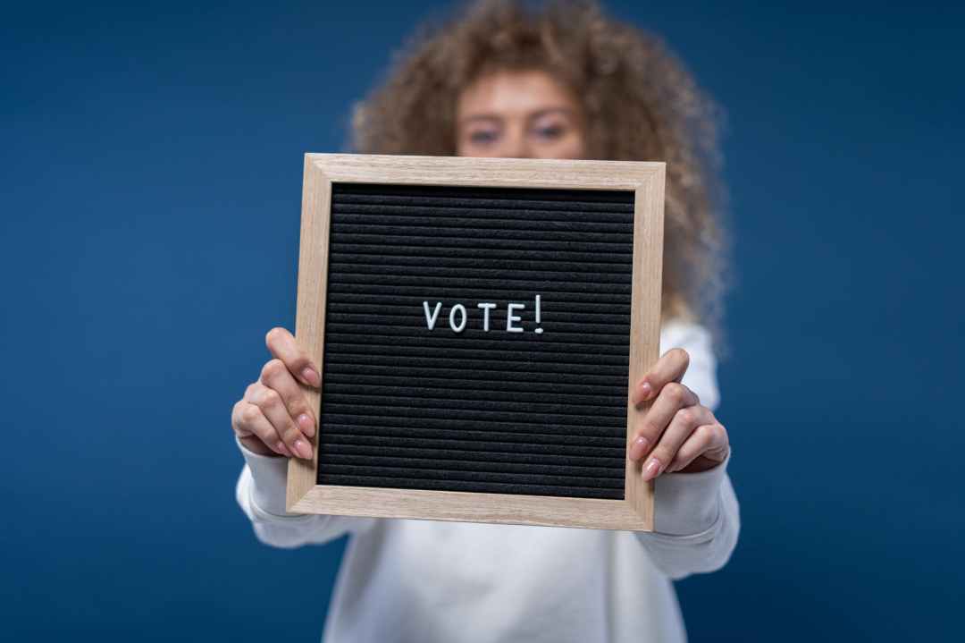 Woman holding sign saying "vote" atop a blue background