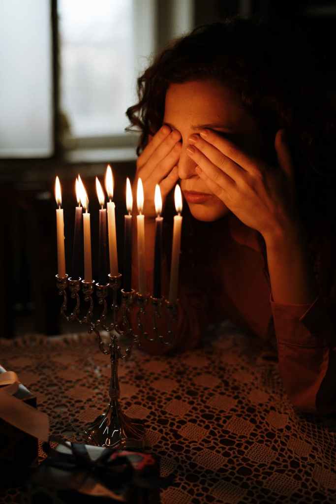 Woman covering her eyes in front of lit candles. 