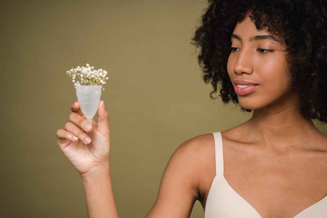 A woman holds a menstrual cup with white flowers coming out of it.