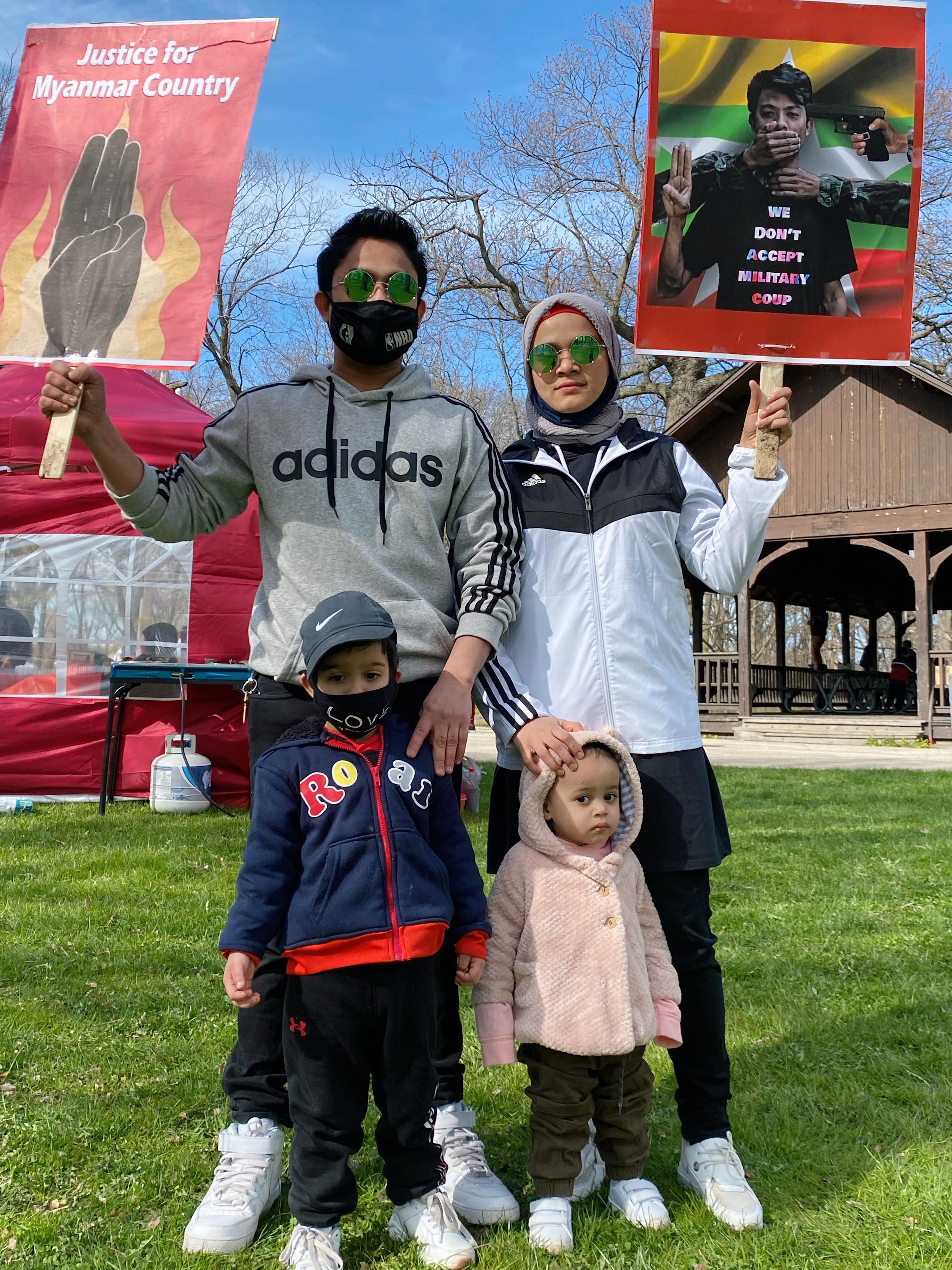 A Rohingya family of four holds signs demanding justice for Myanmar. They are dressed for Chicago spring weather.